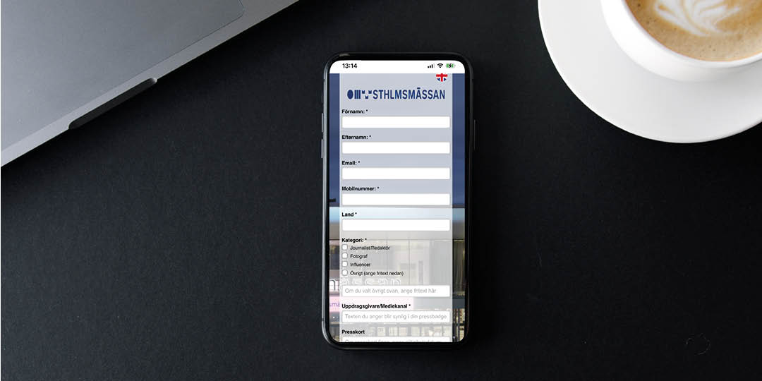 Smartphone visar formulär från Stockholmsmässan, ligger bredvid kaffe.