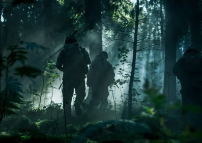 Three soldiers from the Armed Forces move through a misty forest with rays of light breaking through the trees.