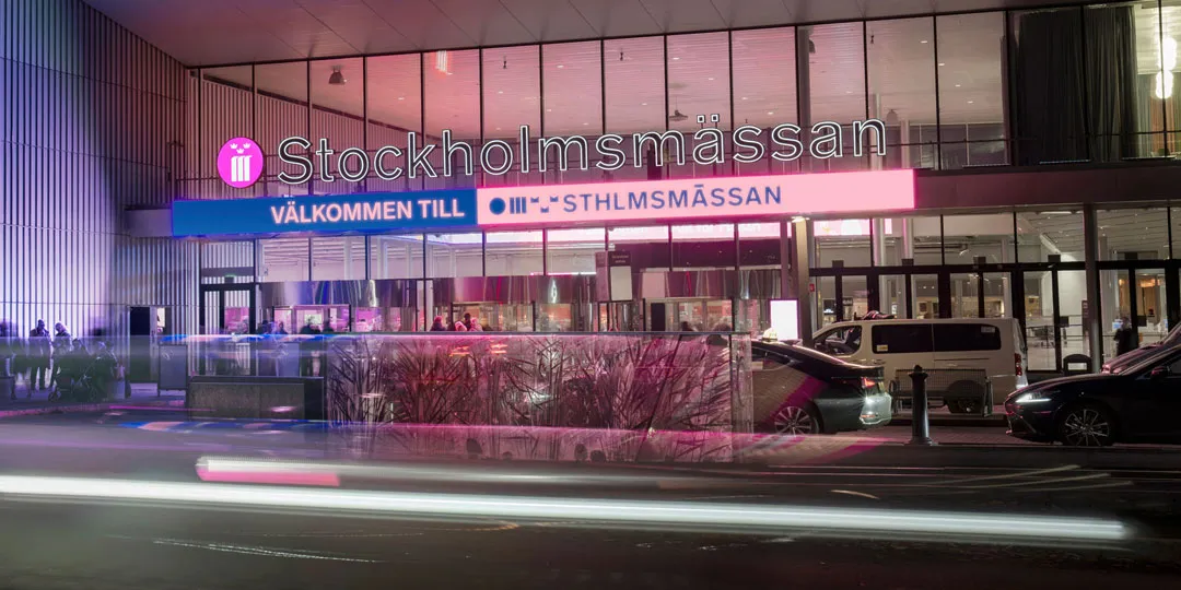 Huvudentrén till Stockholmsmässan upplyst på kvällen.