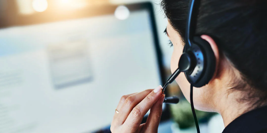 Kontakta oss_iStock-938430346_1080x540 Person wearing a headset working at a computer, providing customer service or support.